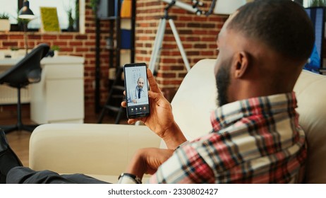 Patient lying on couch remotely discussing treatment plan with doctor during online video call meeting after medical checkup. Man receiving prescription from general practitioner in telemedicine call - Powered by Shutterstock