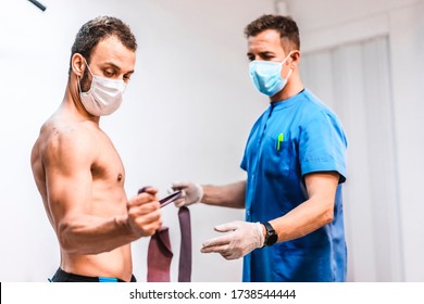 A Patient In A Mask With Arm Exercises With The Physical Therapist. Physiotherapy With Protective Measures For The Coronavirus Pandemic, COVID-19. Osteopathy, Therapeutic Chiromassage