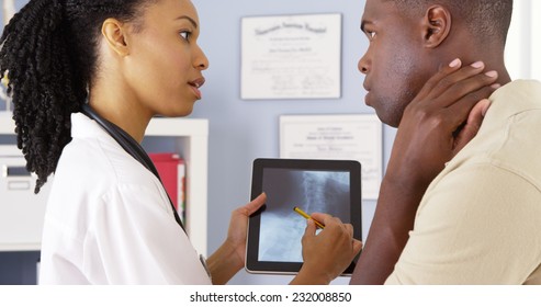 Patient With Neck Pain Talking To Female Doctor About X Ray On Tablet