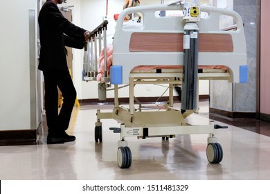 A Patient On A Hospital Stretcher Bed Waits By The Elevator As He Is Being Transported From The Ward For Medical Treatment By A Medical Concierge Attendant Or Assistant At A Private Hospital.