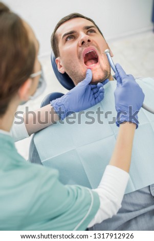 patient with opened mouth near dentist holding dental drill