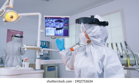Pov de odontólogo paciente hablando de forma encubierta sobre la higina bucal mostrando rayos X en el monitor. Especialista en estomatología con traje protector contra la infección por coronavirus apuntando a la radiografía.