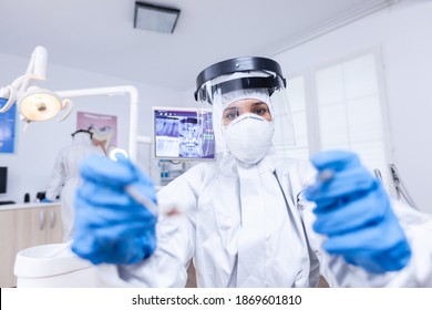 Patient Pov Of Dentist Examining Patient Gums Using Tools Dressed Up In Covid Suit In Dental Office. Stomatolog Wearing Safety Gear Against Coronavirus During Heatlhcare Check Of Patient.