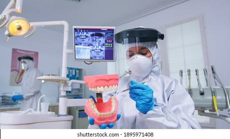 Pase de odontólogo que muestra la forma correcta de limpiar los dientes con precaución contra el covid en la odontología utilizando un accesorio de esqueleto. Estomatologo llevando equipo de seguridad durante la comprobación del cuidado de la salud