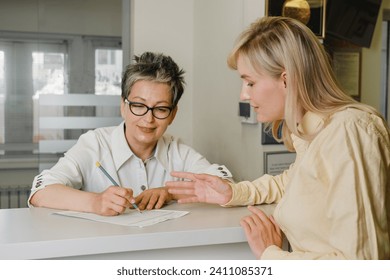 Patient at reception desk of clinic talking about her appointment. Female receptionist taking application form from customer at health care center - Powered by Shutterstock