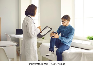 Patient Sitting On Hospital Examination Couch Asks Doctor To Examine His Injured Knee And Prescribe Treatment. Man Telling Doc About Pain, Kneecap Inflammation, Strain, Ligament Sprain, Damaged Tendon