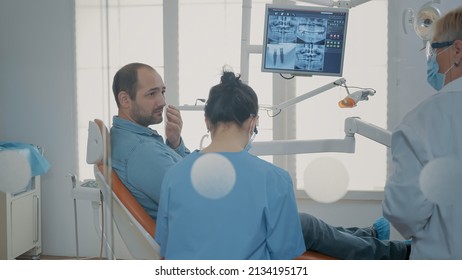 Patient with toothache attending stomatological consultation with dentist and nurse in oral care office. Assistant talking to man about dentition procedure and orthodontic work.