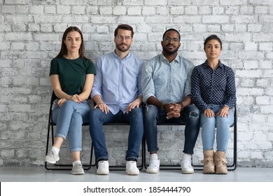 Patient waiting. Group portrait of four diverse people young men and women of different races sitting on chairs along the wall looking at camera expecting turn to visit doctor pass exam job interview