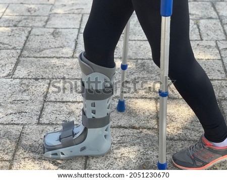 Patient walking with the orthopedic boot ideal for leg injuries, tibia or fibula fracture. Helped by crutches while going to the hospital to be treated by doctors. Orthopedic medical concept.