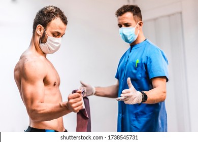 A Patient Without A Shirt And Wearing A Mask With Arm Exercises With The Physical Therapist. Physiotherapy With Protective Measures For The Coronavirus Pandemic, COVID-19. Osteopathy, Therapeutic Chir