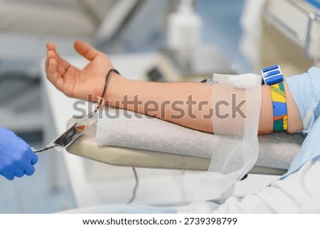 Patient's arm with a needle inserted, undergoing blood donation for medical purposes, supporting healthcare and charity