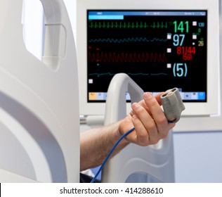 Patient's Hand in Bed with Oximeter and Monitor on Background