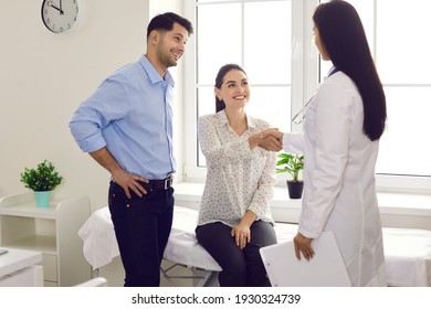 Patients thanking their family doctor for help. Smiling married couple shaking hands with medical worker. Happy young spouses planning pregnancy and consulting specialist at office of modern hospital