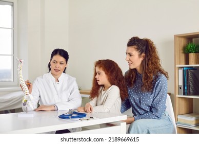 Patients Visit Doctor At Orthopedic Clinic. Female Medic Shows Anatomical Spine Model. Mum And Child Listen To Specialist Tell About Spinal Scoliosis Curvature And Back And Skeleton Problem