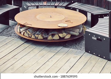 Patio Fire Pit Table For Outdoor Leisure Party On The Wood Deck Terrace. Iron Rounded Fire Pit With Grill Top On Backyard Party Place. Grill Appliance And Fireplace On The Back Yard Lawn.