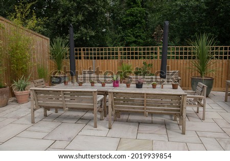 Patio Paved with Indian Sandstone Slabs, Teak Table and Benches with Succulent Plants in Flowerpots and a Wooden Fence and Woodland Background in a Garden in Rural Devon, England, UK