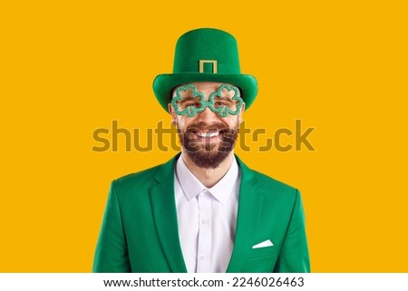 Patricks Day. Red-haired man in green suit is classic hero of national Irish holiday. Cloverleaf decorative eyewear on wide smiling face. Green carnival costume. Isolated on yellow background.