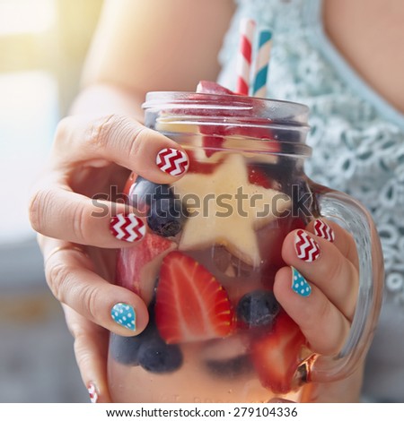 Patriotic drink cocktail with strawberry, blueberry and apple in woman's hands