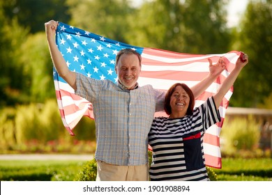 Patriotic family holding the usa flag outdoors. Happy aged caucasian couple holding the usa flag on the green background. - Powered by Shutterstock