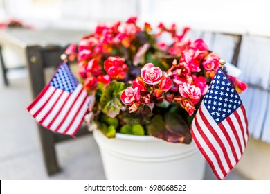 Patriotic flower pot with American flags and pink or red begonia flowers on porch