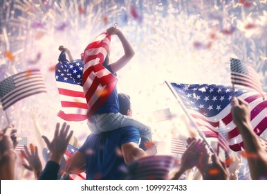 Patriotic holiday. Child sitting on shoulders of her father and  holding the Flag of the USA. America celebrate 4th of July.