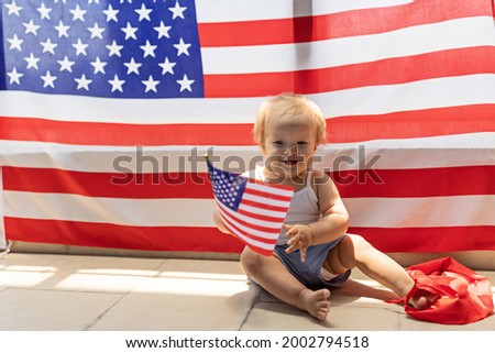 Patriotic holiday. Cute caucasian baby ten-eleven months old with blonde hair and blue eyes with American flag at home. USA celebrate independence day 4th of July.