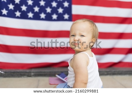 Patriotic holiday. Cute caucasian baby ten-eleven months old with blonde hair and blue eyes with American flag at home. USA celebrate independence day 4th of July.