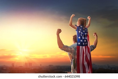 Patriotic holiday. Happy family, father and his daughter child girl with American flag outdoors on background sunset cityscape. USA celebrate 4th of July.
