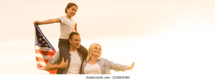 Patriotic Holiday. Happy Family, Parents And Daughters Children Girl With American Flag Outdoors. USA Celebrate 4th Of July.