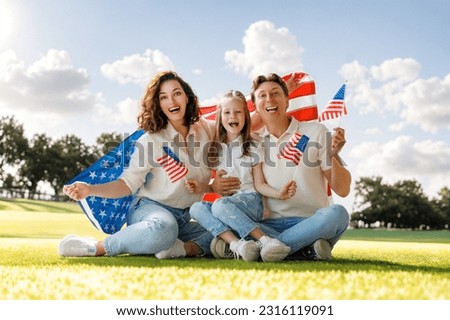 Patriotic holiday. Happy family, parents and daughter child girl with American flag outdoors. The USA celebrate 4th of July.