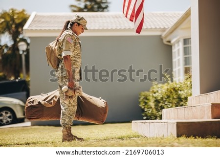 Patriotic military mom holding a teddybear while standing outside her house with her luggage. American female soldier coming back home after serving her country in the army.