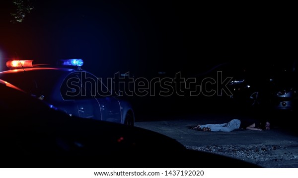Patrol car with flashing lights standing near\
victim of crime, lying on\
street