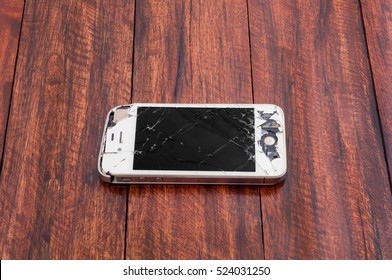 PATTAYA, THAILAND - 28 NOVEMBER 2016: Studio shot of broken mobile phone iPhone 4S with damaged screen and body on dark wooden table surface with selective focus. iPhone mobile designed by Apple