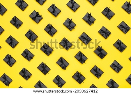 Pattern with black gift boxes with black ribbons on bright rich yellow background. Black Friday sale flat lay, top view. Discount, advertising and sale concept. Creative minimalist design