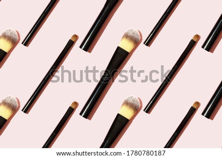 A pattern of black makeup brushes. Modern bright decorative background. Women's accessories on a pink background. Professional makeup artist's tool for applying eyeshadow and foundation