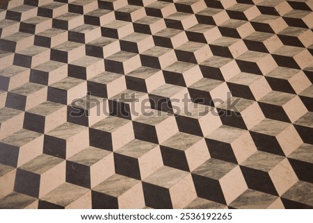 A pattern of brown and white squares is on a wooden surface. The squares are arranged in a way that creates a sense of depth and dimension.