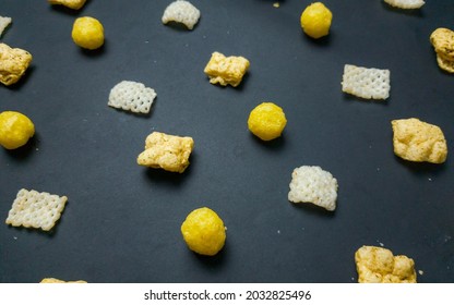 Pattern Of Cheese Puffs And Chip And Crackers On Black Background Viewed From Side