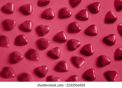 Pattern of chocolate sweets as heart in foil. Trending color of 2023 - Viva Magenta.