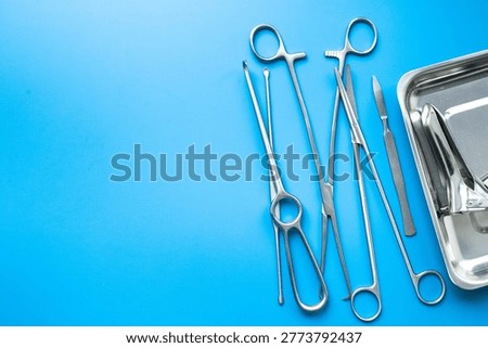 Pattern flat lay of stainless surgical instruments and tools on blue table, top view.