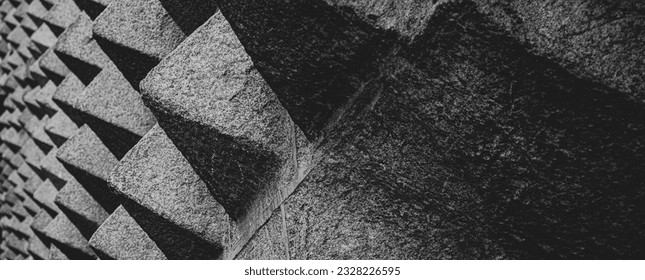 Pattern of granite textured stone pyramid shapes covering the wall on the facade of La Casa de los Picos de Segovia on Juan Bravo street with the balcony in the background.