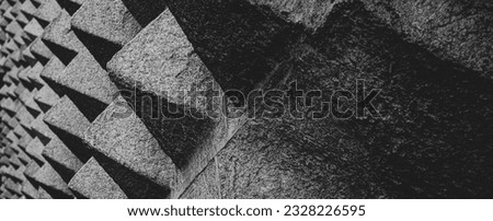 Pattern of granite textured stone pyramid shapes covering the wall on the facade of La Casa de los Picos de Segovia on Juan Bravo street with the balcony in the background.