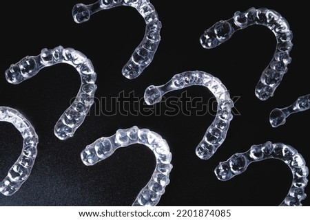 a pattern of invisible plastic aligners lie on a black background