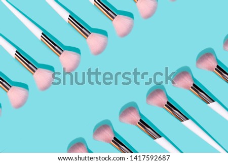 Pattern made of make up white brush on turquoise background. Minimal beauty concept.