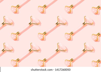 Pattern made with pink Gua Sha massage tools. Rose Quartz jade roller on pink background. Anti age, lifting and toning treatment at home. Copy space.