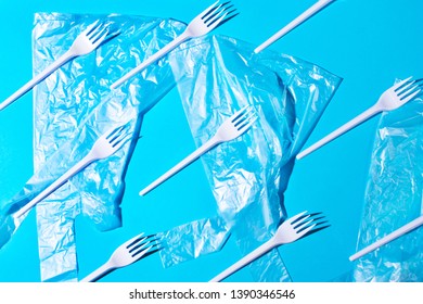 Pattern of many white plastic forks and transparent bags with dark shadow on blue background. Concept of saving the planet and environment. Flat lay minimalistic style.