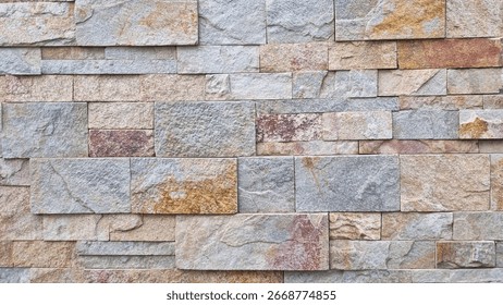 Pattern of rectangular natural stone tiles in mixed earthy tones forming a stacked wall texture. Stone cladding surface photography. Construction background concept
