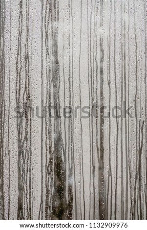 Pattern of streaks caused by rain on steamy window of tropical greenhouse (shallow depth of field), for motifs of humidity and climate control, visibility, the environment 