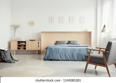 Patterned Armchair In Bright Bedroom Interior With Wooden Cupboard Next To Blue Bed. Real Photo