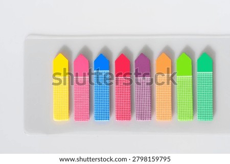 Patterned arrow sticky notes on transparent plastic holder white background. Vibrant multi colored adhesive index tabs with grid dots design arranged in a row for document organization bookmarking or office supply.
