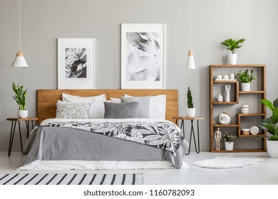 Patterned blanket on wooden bed between tables with plants in bedroom interior with posters. Real photo